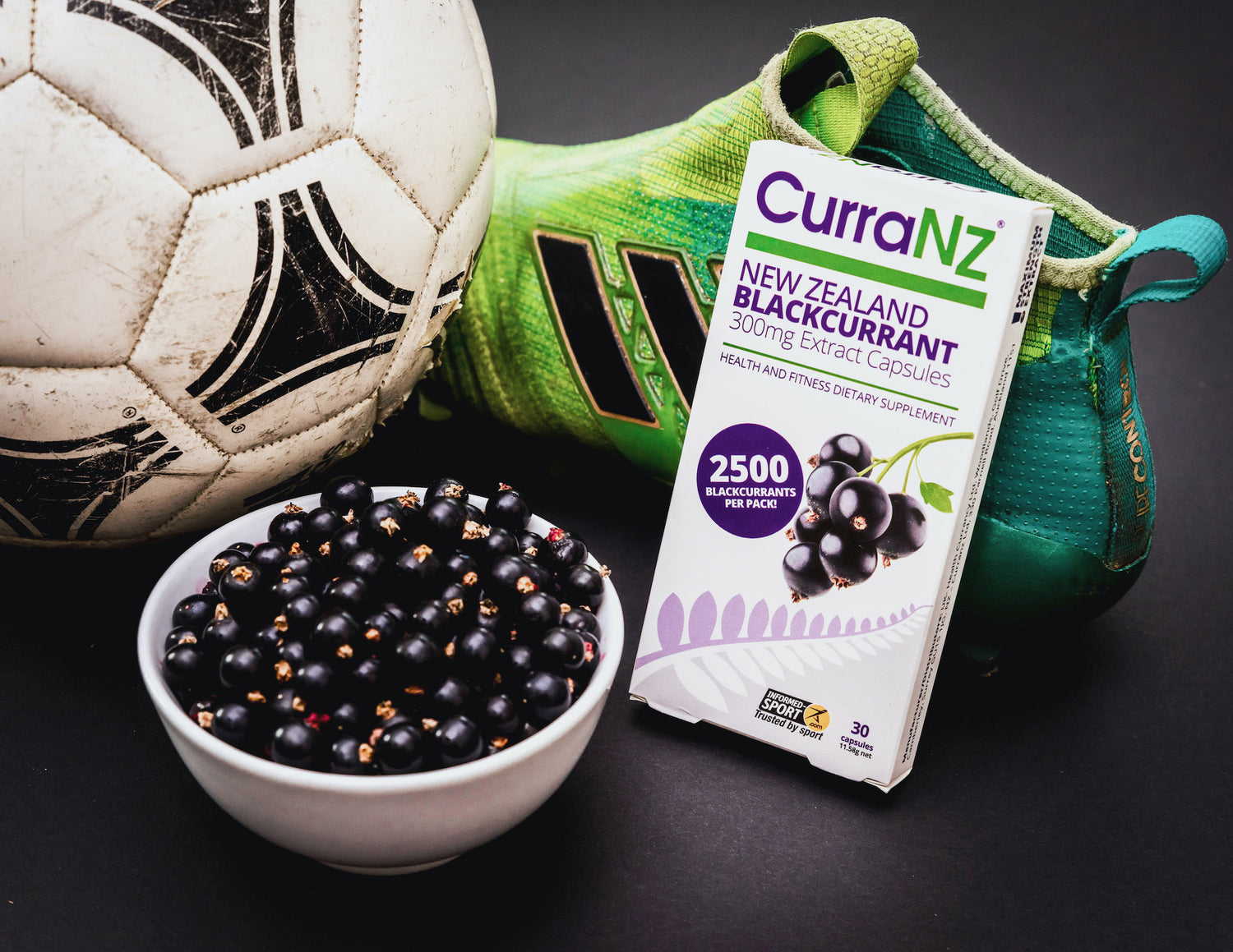 A packet of CurraNZ® sitting beside a bowl of New Zealand blackcurrants and football gear.